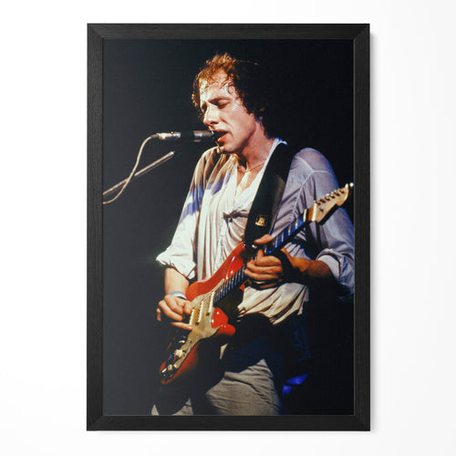 Mark Knopfler singing on stage with his red guitar in 1978, color photo in a classic black poster frame