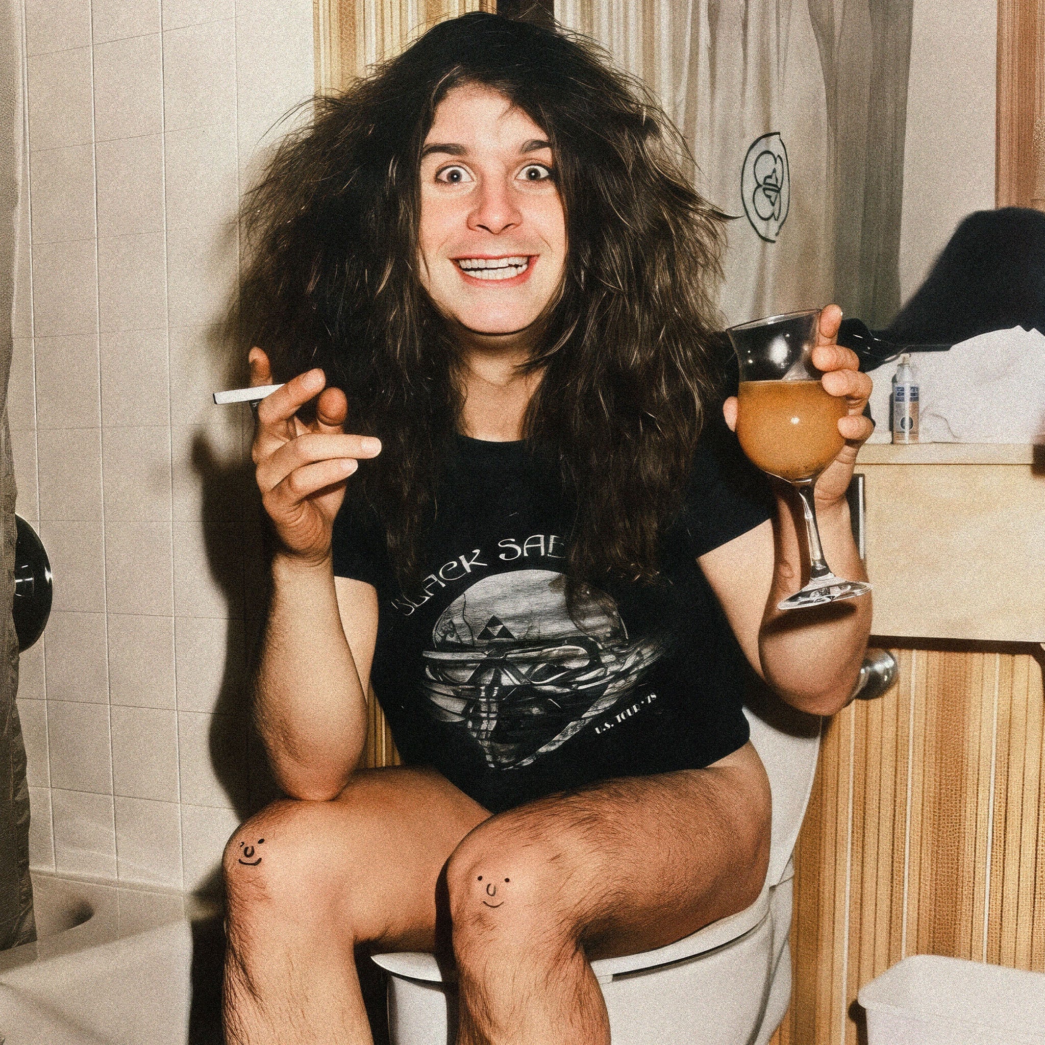 Zoomed detail of Ozzy Osbourne with his drink, cigarette and smiley-face knees, 1978