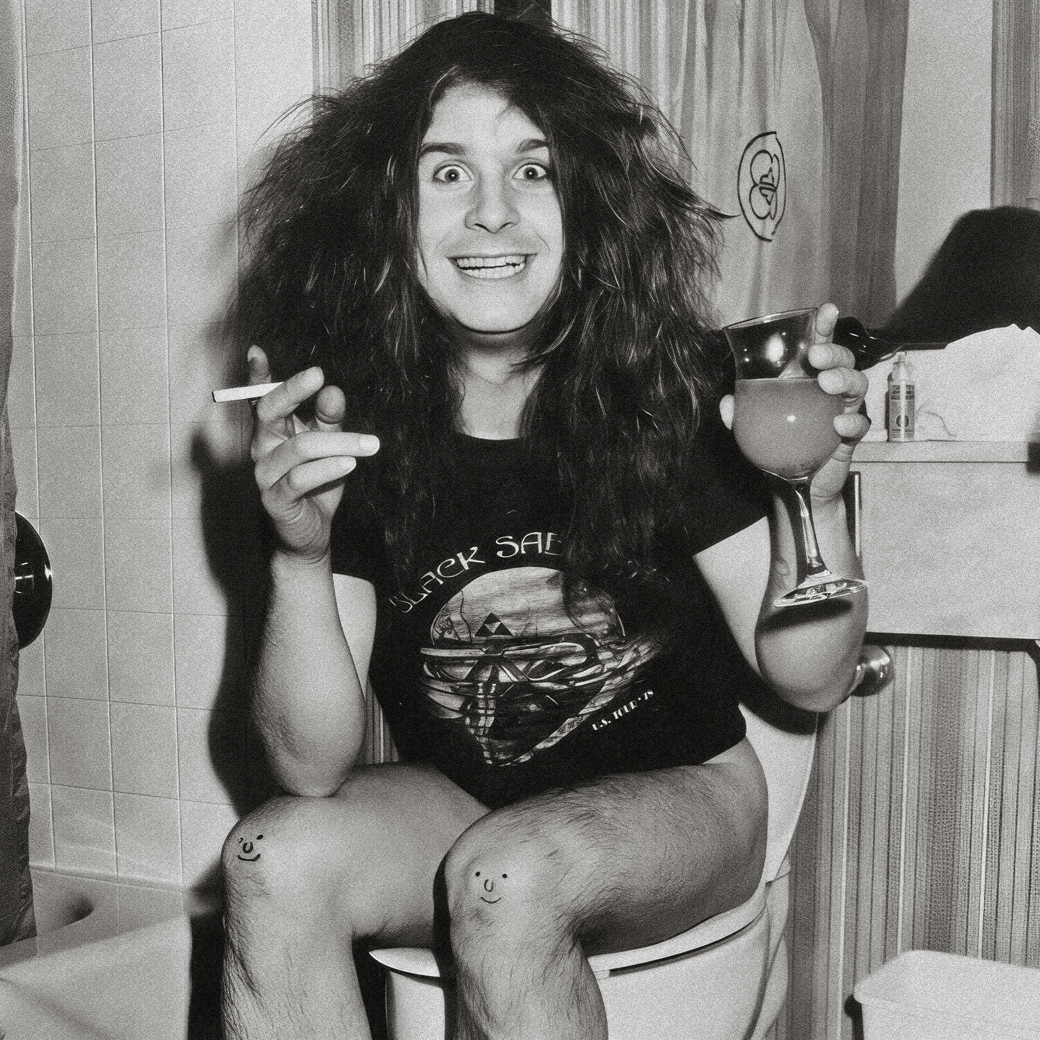 Zoomed detail of Ozzy Osbourne with his drink, cigarette and smiley-face knees in black and white, 1978